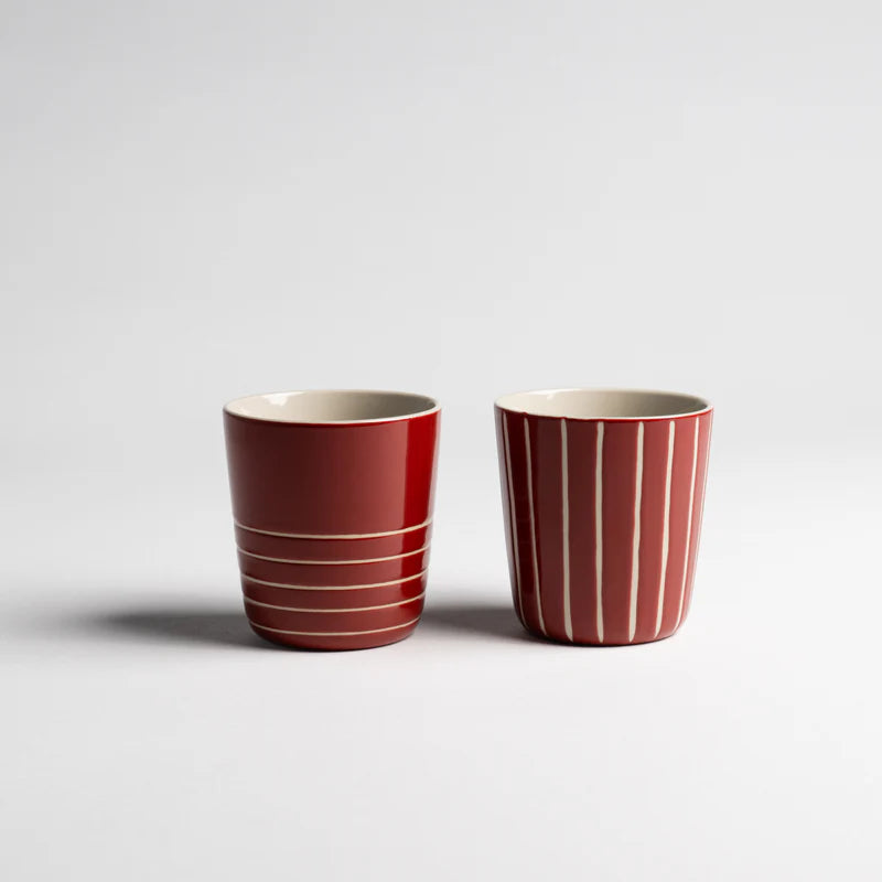 Two red ceramic cups with white stripes on a light gray background