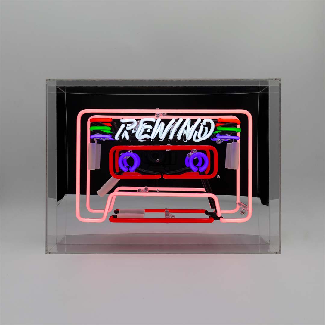 Neon sign shaped like a cassette tape with 'REWIND' text inside a clear box on a grey background
