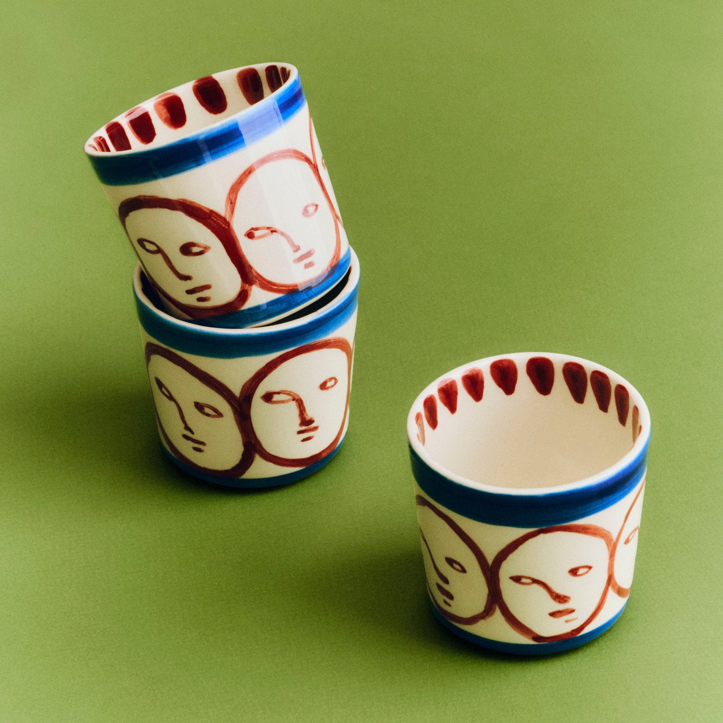 Stack of ceramic cups with face designs on a green background