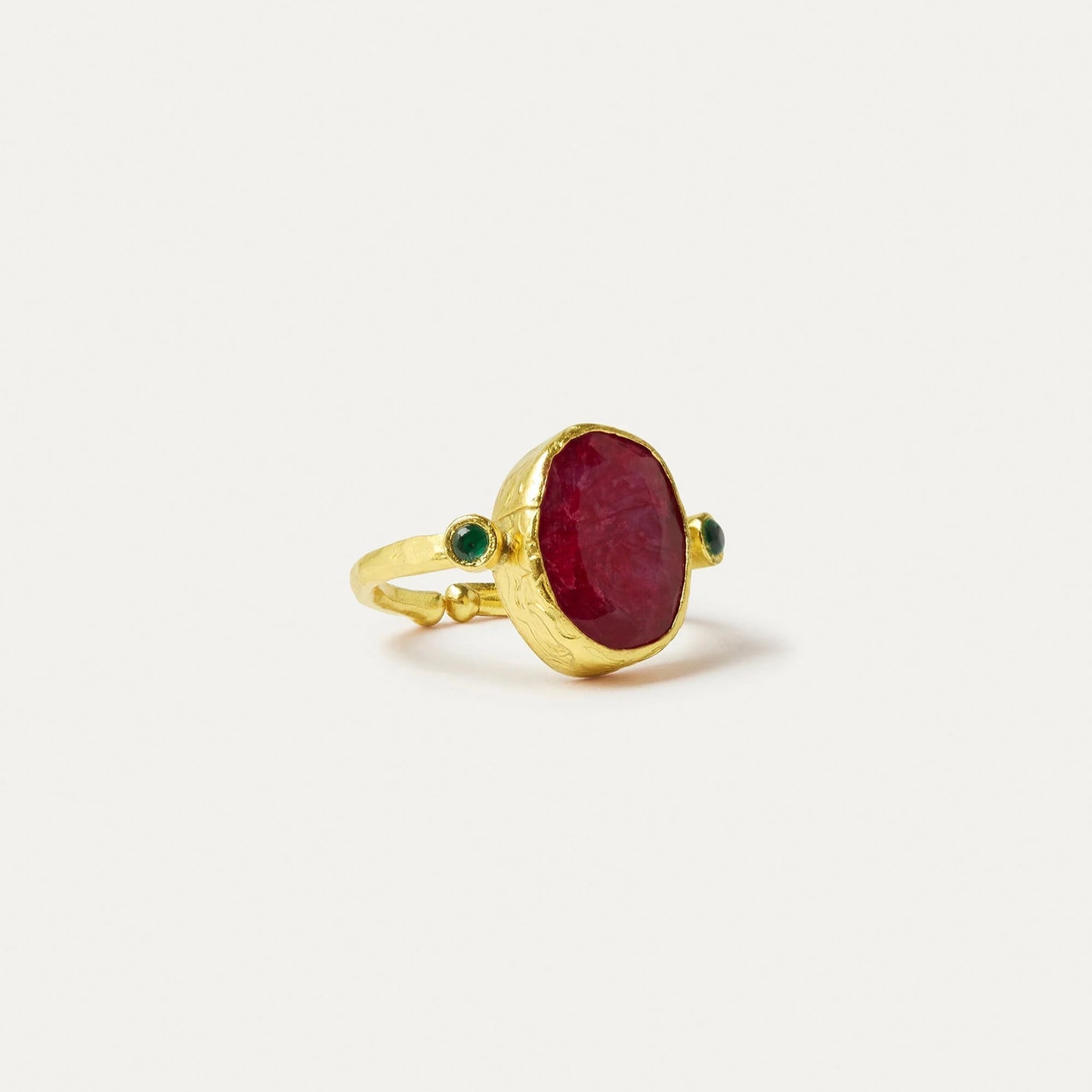 Gold ring with a red stone and green accents on a white background