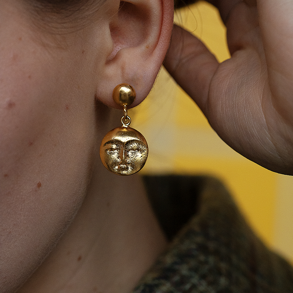 
                  
                    A person wearing a moon face gold drop earring.
                  
                