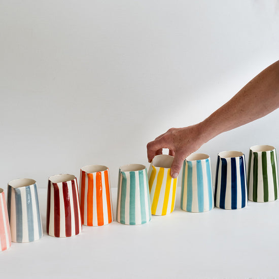 Multiple ceramic, stripe design coffee creamers lined up in a line.