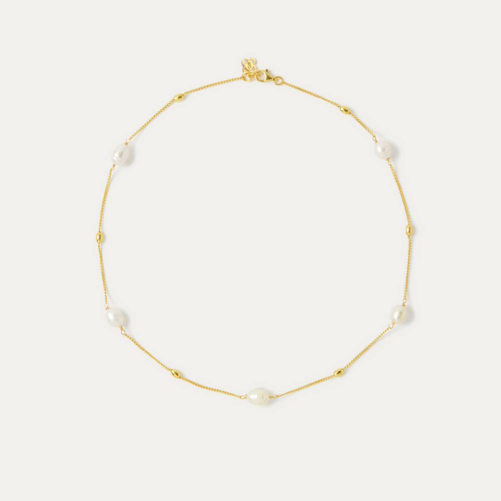 A necklace on a thin gold chain featuring five white pear beads spread around the necklace chain.