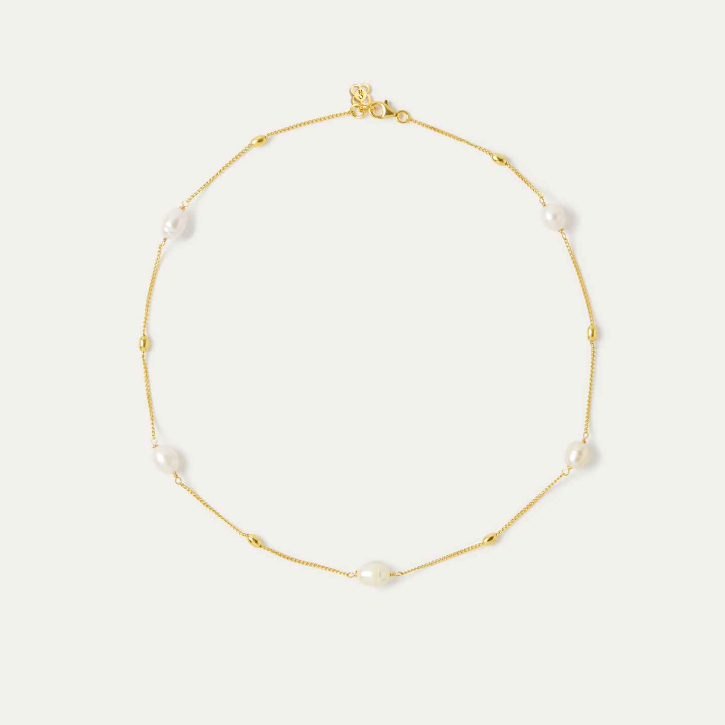 A necklace on a thin gold chain featuring five white pear beads spread around the necklace chain.