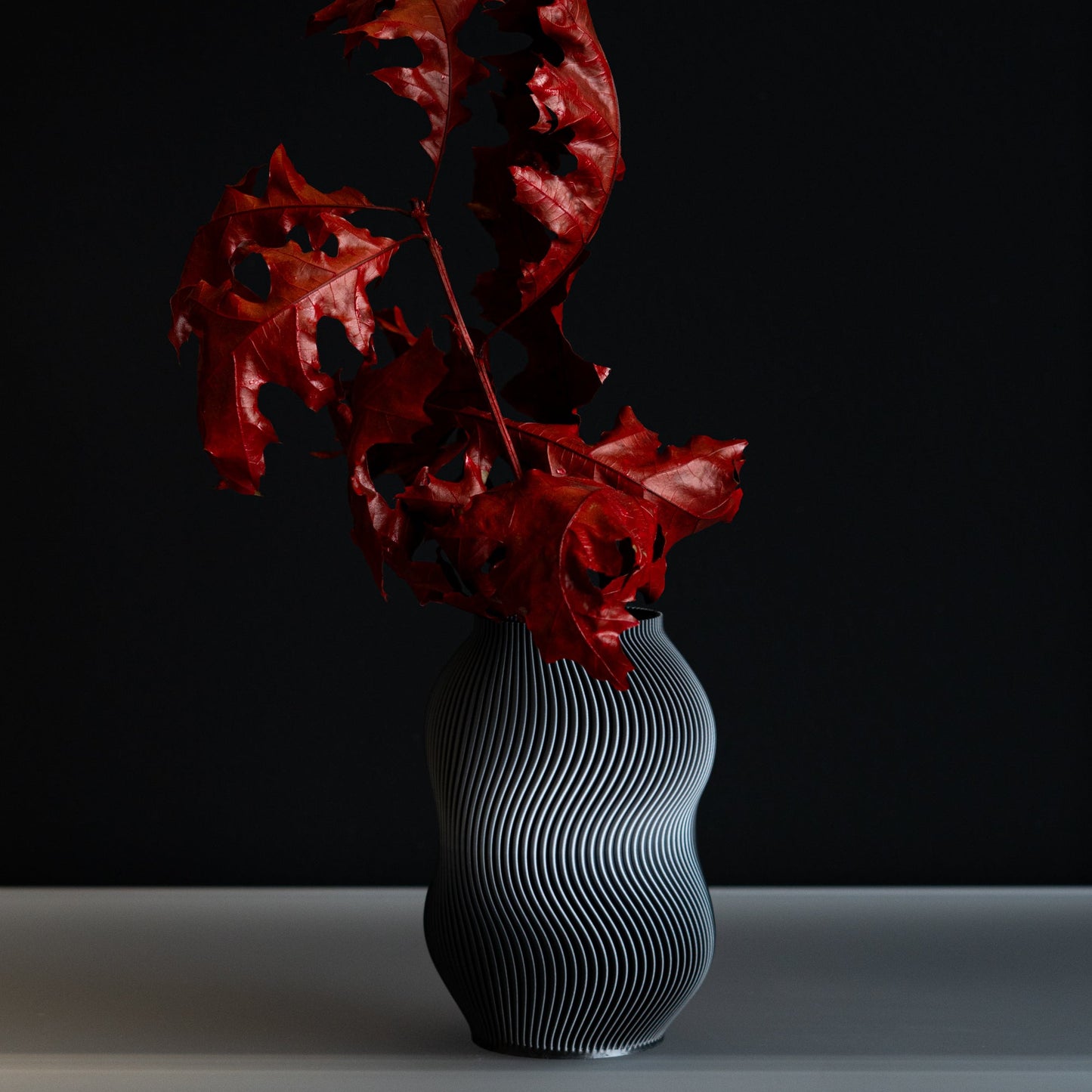 Gray textured vase with red leaves against a black background
