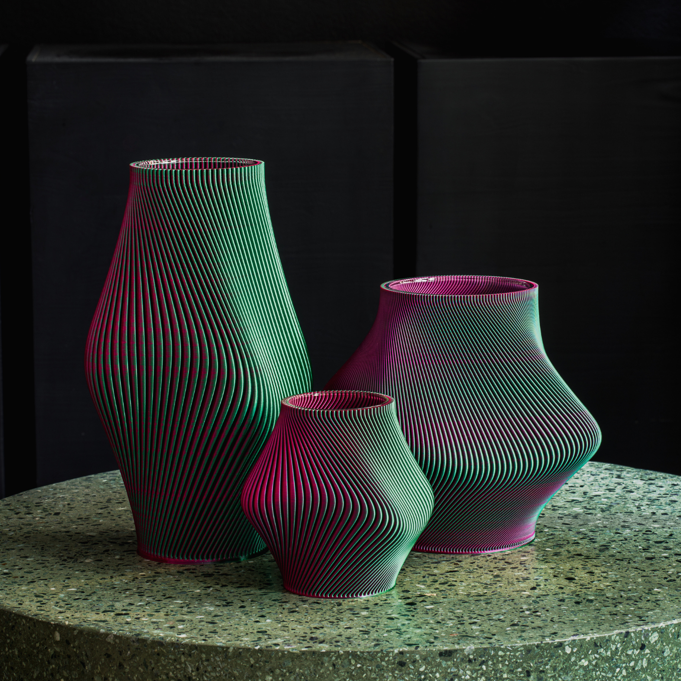 A lifestyle group shot of three 3D printed vases of different sizes on a stone round table.