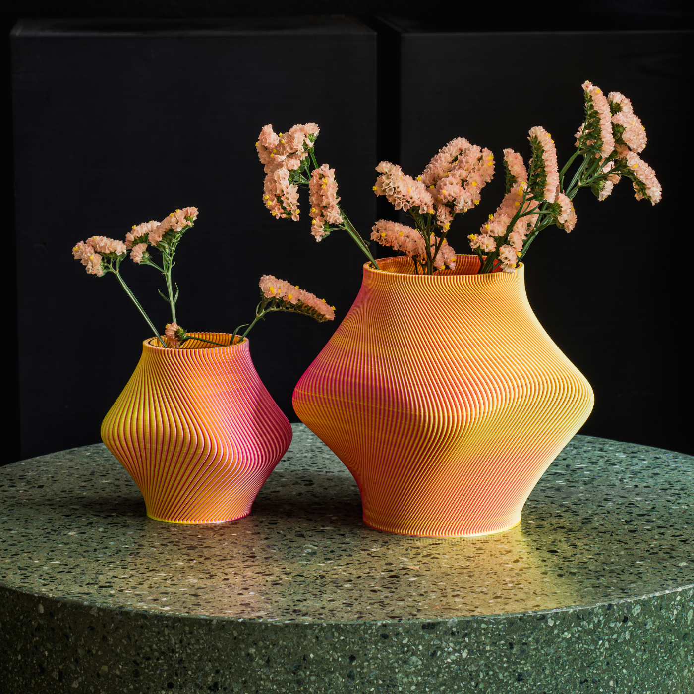 Two orange 3D printed short vases filled with flowers, placed on a stone round table.