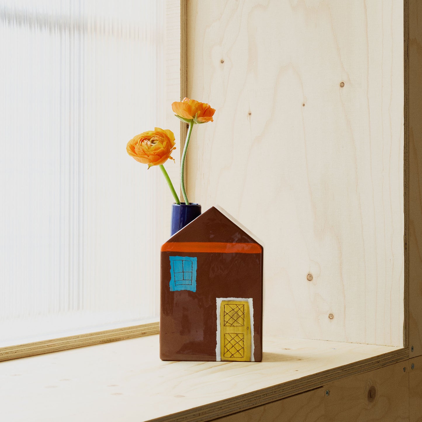 House-shaped vase with colourful design on a wooden shelf