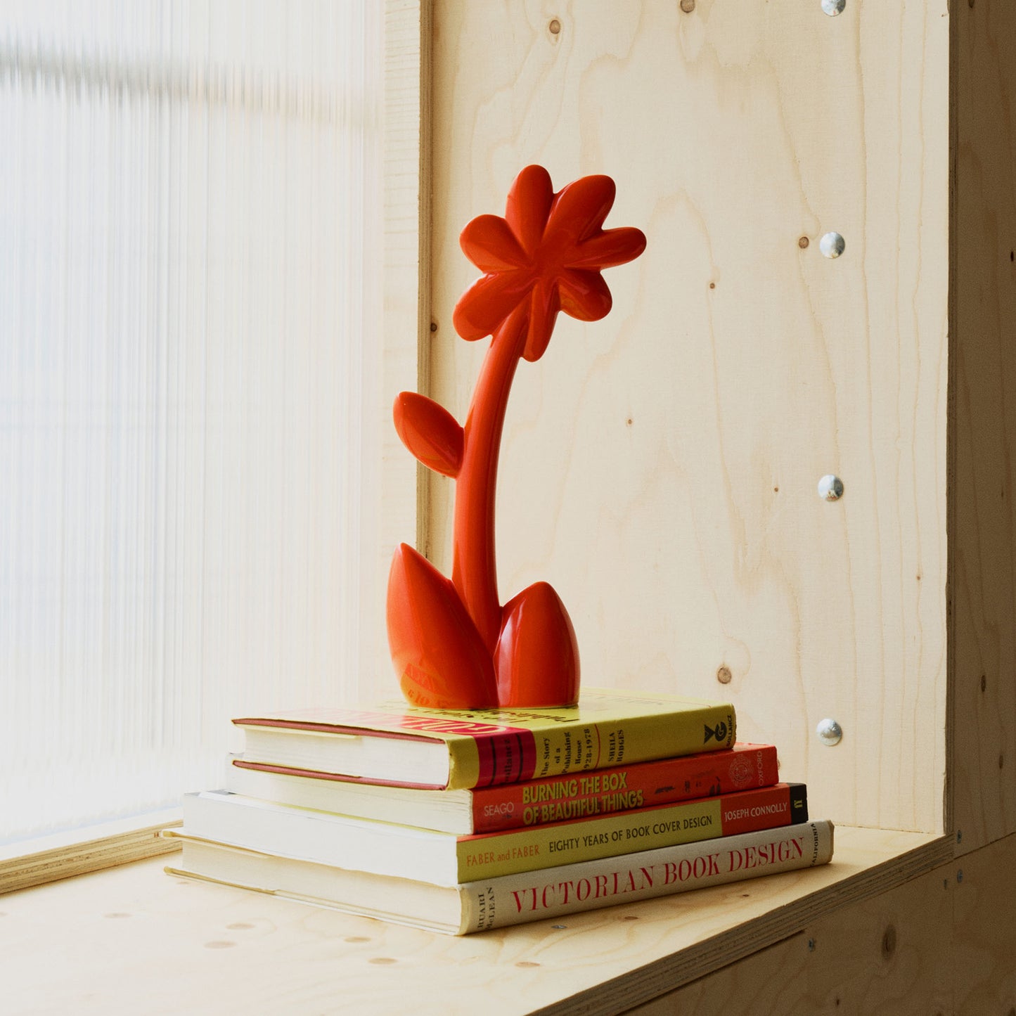 Red ceramic flower sculpture on a stack of books with a wooden shelf background