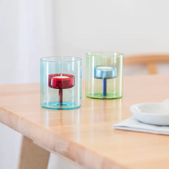 two glass tealight holders sitting on a table.