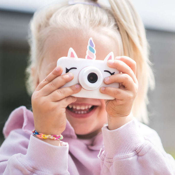 Child holding a unicorn-themed camera up to their face outdoors