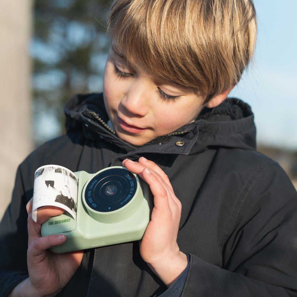 Child holding a green camera outdoors on a clear day