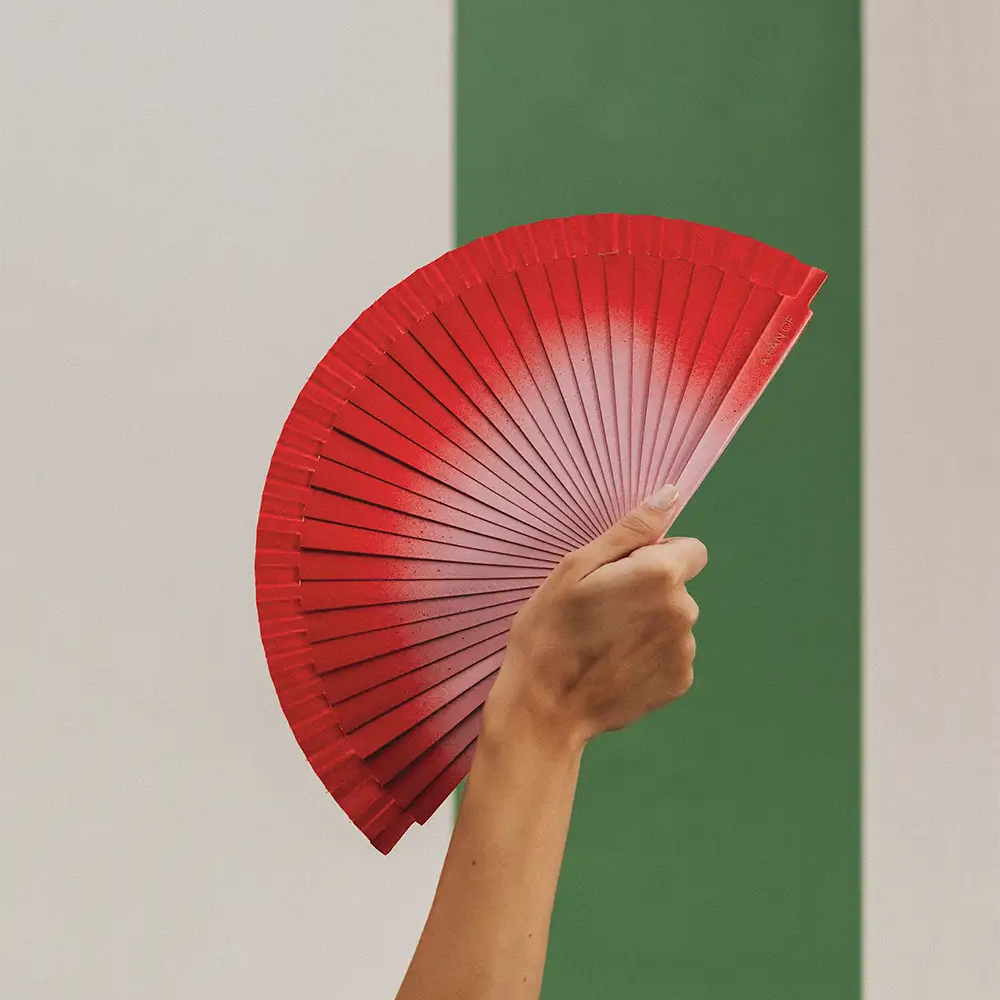 Hand holding a red fan against a green and beige striped background