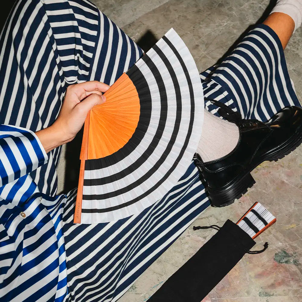 Person holding a black and white striped fan with an orange center on a concrete floor.