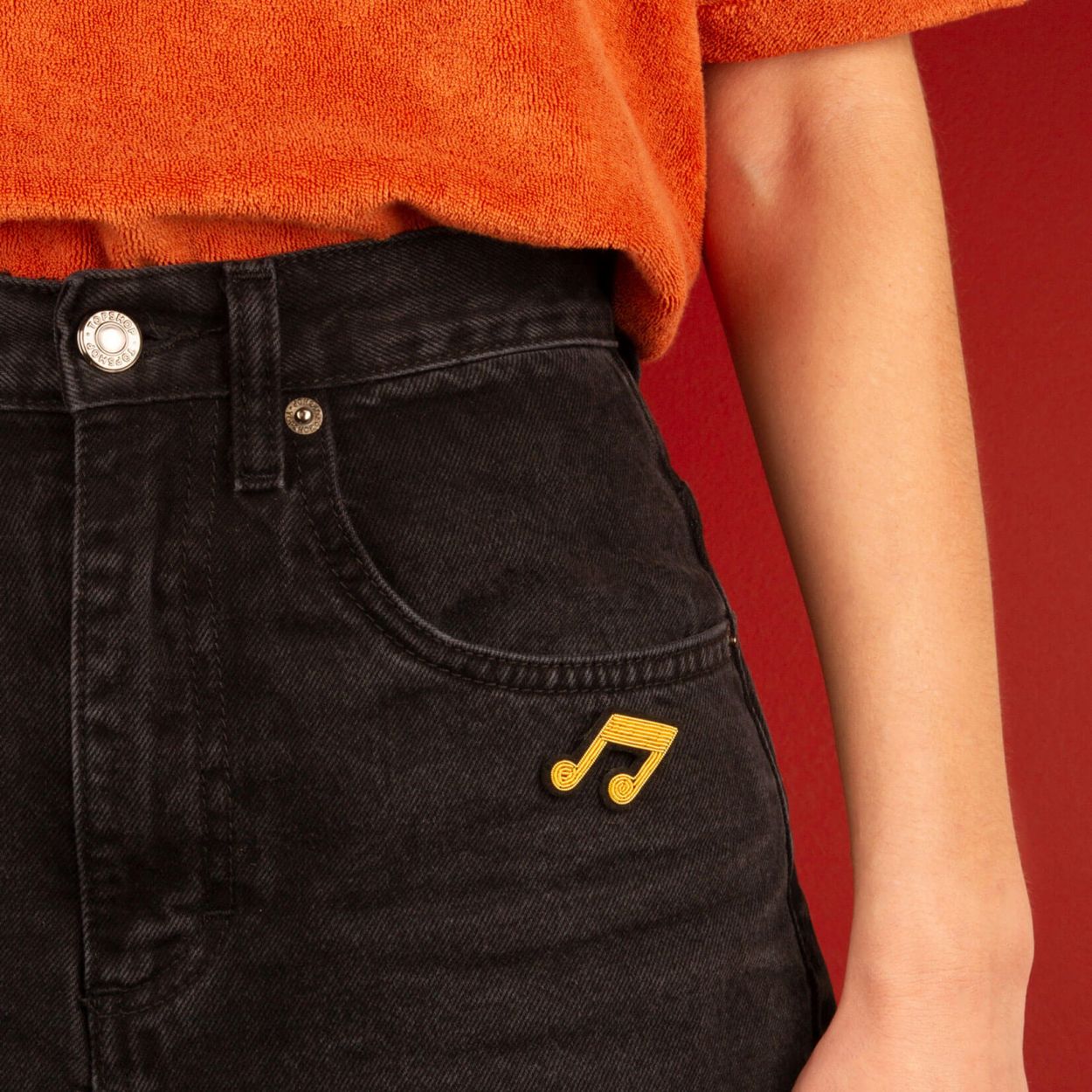 An embroidered music note brooch attached to a person's jeans.