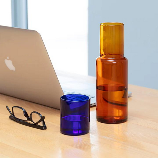 water carafe with glass on desk with pair of glasses.