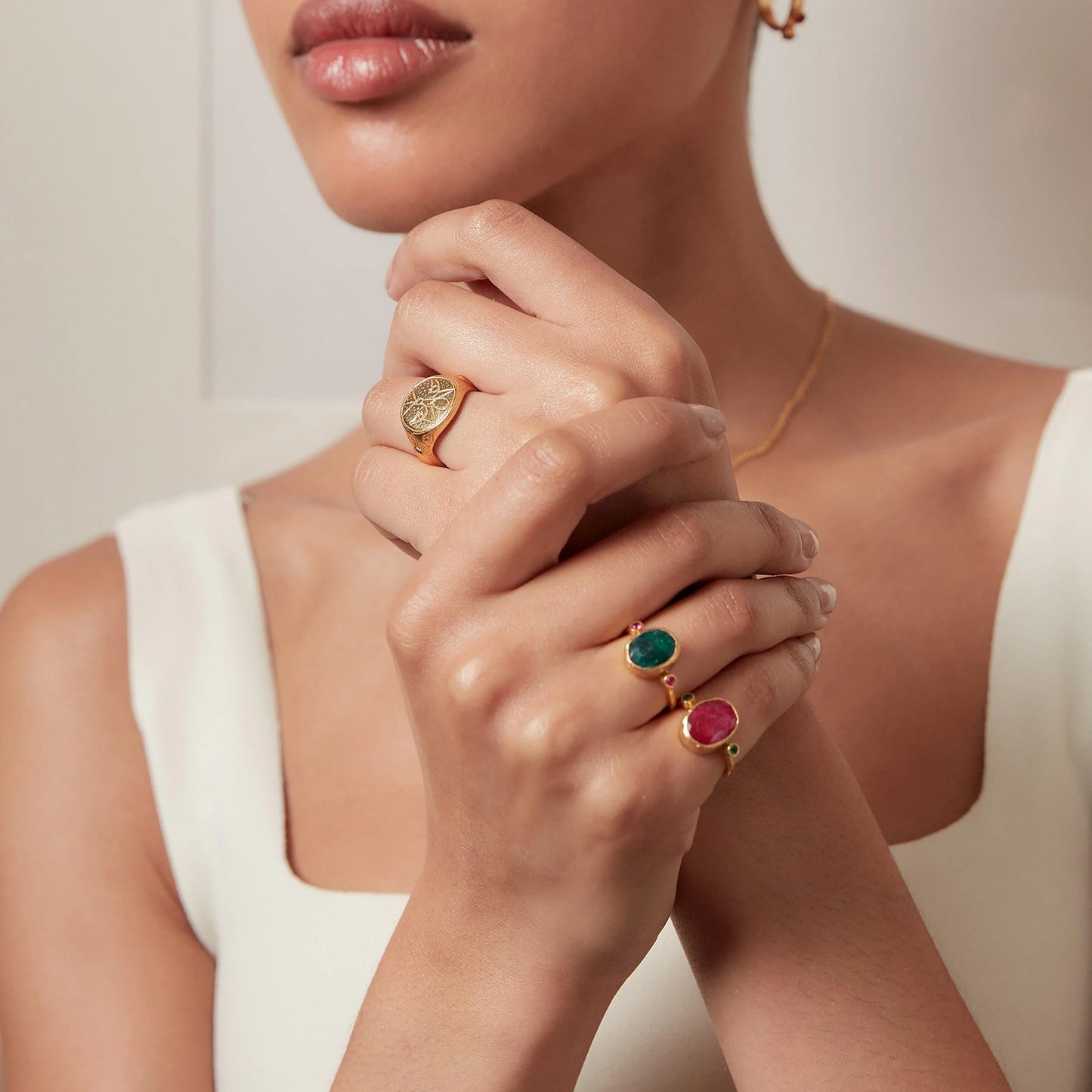 Woman wearing gold rings with colorful gemstones on a neutral background