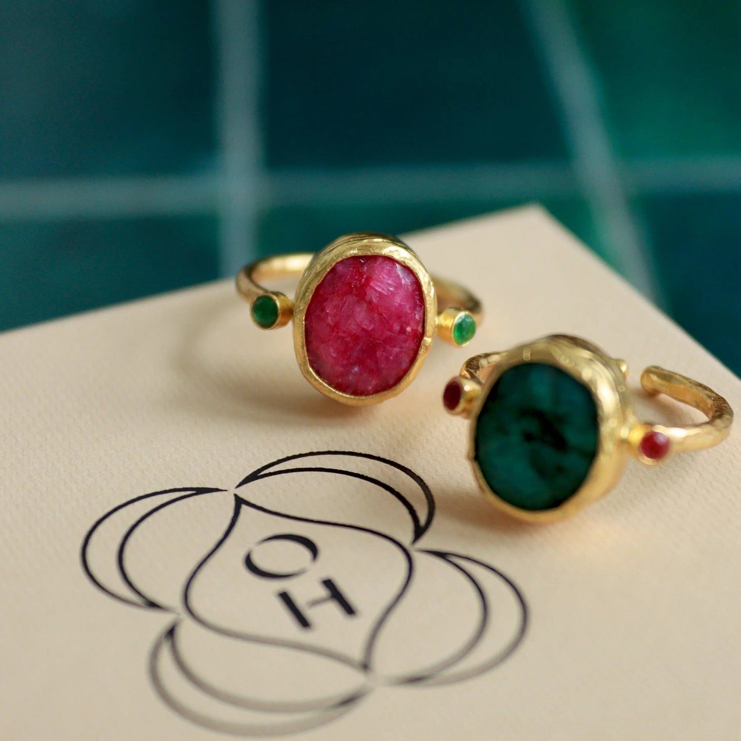 Two gold rings with gemstones on a card with a logo