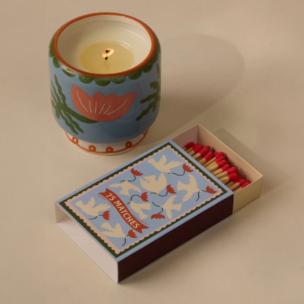 Ceramic candle with decorative design next to a box of matches on a beige background