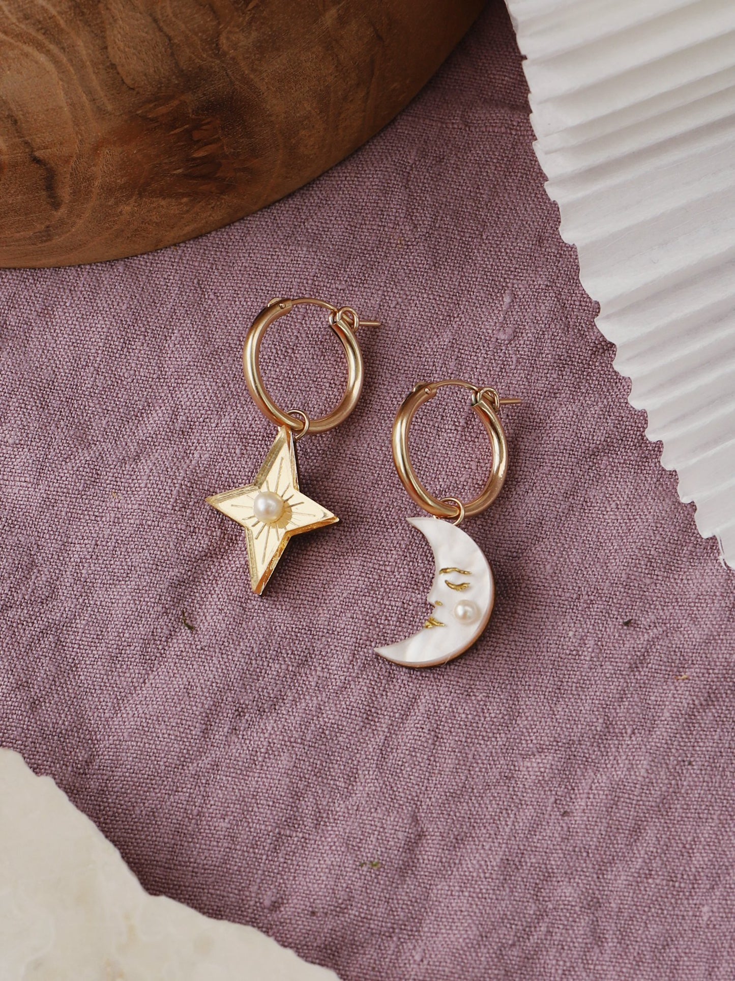 A pair of mis-matched gold hoop earrings, one has a gold star pendant with a pearl in the centre and the second earring has a crescent moon pendant hanging from the hoop.