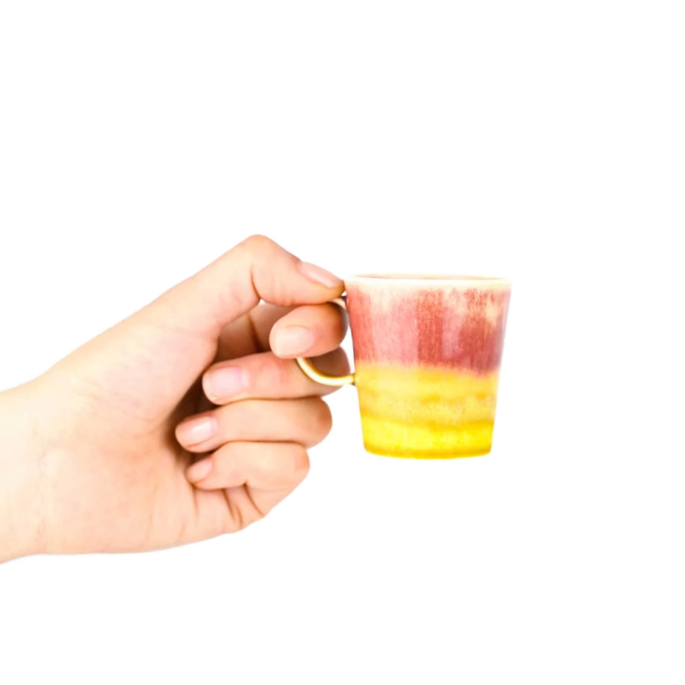 Hand holding a small ceramic cup with a gradient design on a white background