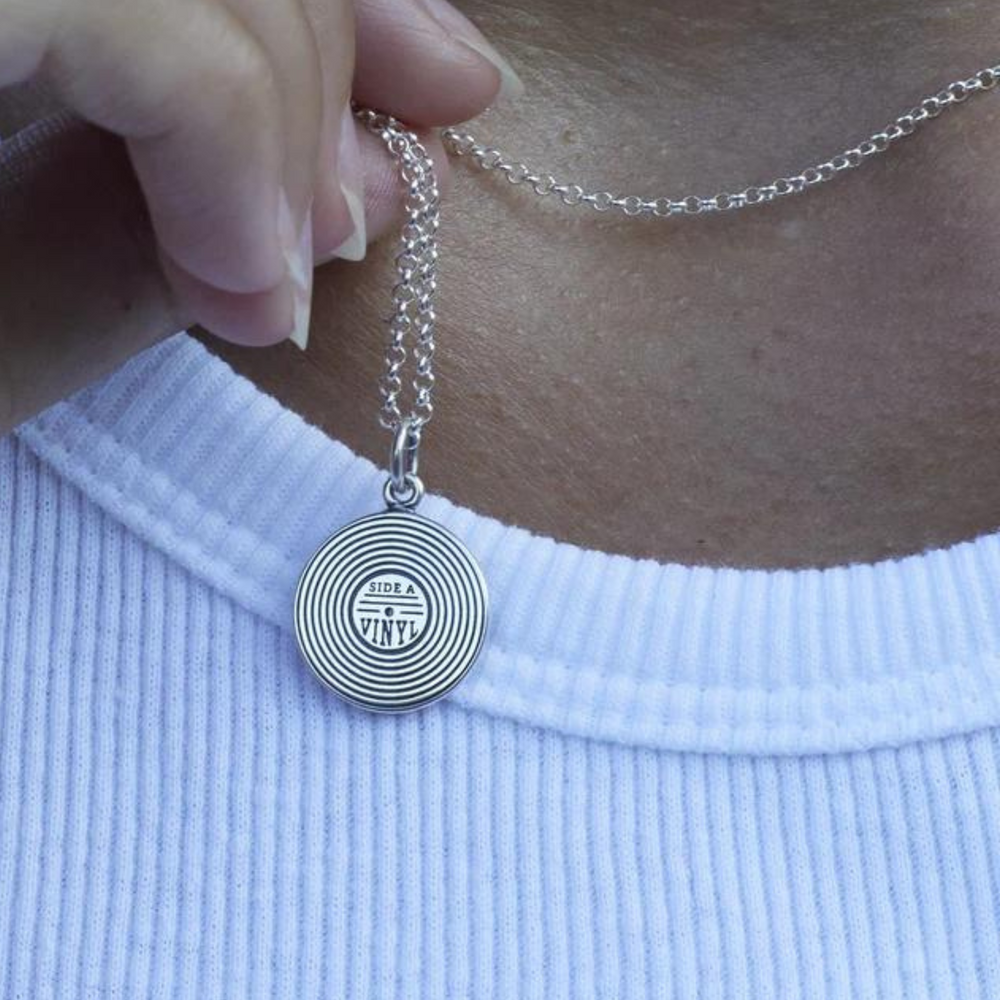 
                      
                        hand holding silver necklace with vinyl charm against neck.
                      
                    